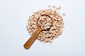 A pile of spelt flakes with a wooden spoon on a white surface