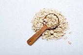 A pile of oats with a wooden spoon on a white surface