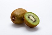 A whole kiwi and a halved kiwi on a white surface