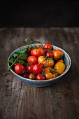 Various types of tomatoes in a bowl on a wooden surface