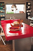 Bright red tabletop in kitchen with crockery on wall-mounted shelves