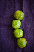 Four green zebra tomatoes on a violet cloth