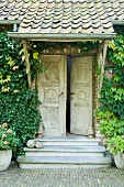 Vintage-style entrance with traditional carved wooden doors, porch and climber-covered façade