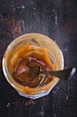 Leftover caramel sauce in a glass jar with a spoon