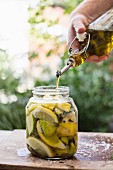Olive oil being poured into a glass jar with pickled lemons