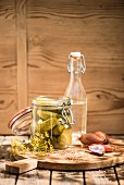Gherkins in a preserving jar, vinegar, shallots, mustard seeds and dill on a wooden board