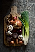 An arrangement of onions, garlic and leeks on a chopping board (seen from above)