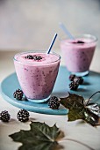 Two glasses of blackberry drinking youghurt with blackberries and autumnal leaves