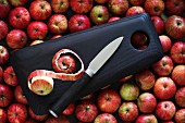 A wooden chopping board with a knife on red apples