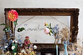 Blumenarrangement mit Vintage Flair vor antikem Bilderrahmen und Handschrift an Wand