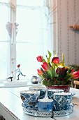 Advent arrangement of red tulips and fir branches in tin can behind tray of cups