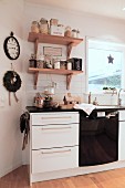 Kitchen base units below storage jars and Christmas decorations on wall-mounted shelves
