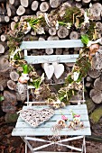 Heart-shaped wreath decorated with flowering bulbs on garden chair in front of stacked firewood
