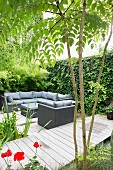 Lounge area on wooden deck next to garden pond and jetty with climber-covered screen wall