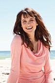 A brunette woman in a pink long-sleeved top on the beach