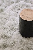 Side table made from black-painted tree stump on fluffy rug