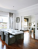 Grey loose-covered chairs around white dining table below window in elegant dining room with sliding door