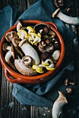 Assorted mushrooms in a clay bowl on a wooden surface