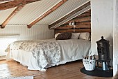 Wood-beaming sloping ceiling and small stove in rustic attic bedroom