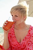 A blonde woman wearing a patterned tunic dress and drinking a smoothie