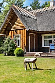 Wooden horse on lawn in front of wooden house with thatched roof