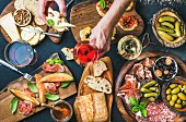 Italienische Antipasti auf Holzbrettern (Brushettas, Käse, Oliven, Gurken, Prosciutto di Parma, Melone, Salami, und Wein)