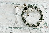 Easter wreath made from box leaves and quail eggs and goose's egg on antique silver spoon on rustic wooden surface