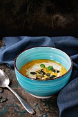 Turquoise ceramic bowl of pumpkin and sweet potato cream soup with fresh basil, cream and seeds
