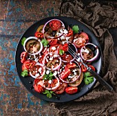 Black plate with sliced different tomatoes, red onion, balsamic sause, parsley and feta cheese salad