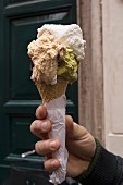 A hand holding an ice cream cone with pistacho & rum ice cream and cream