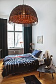 Schlafzimmer mit Doppelbett, Vintage-Nachttischlampe und Hängelampe mit Korbschirm in Altbauwohnung