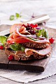 A slice of bread topped with ham, vegetables, lingonberries and chia seeds