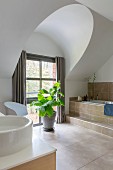 Elegantes Badezimmer mit Steinfliesen, Badewanne und Zimmerpflanze vor dem Fenster