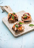 Bruschettas with parma, cream cheese, grilled melon, fresh basil leaves and balsamico on wooden cutting board