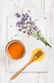 Lavender honey in glass jar and on a honey drizzler next to fresh lavender flowers on ceramic board