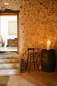 Lit pillar candle on top of old wooden barrel against stone wall