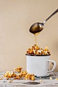 Karamellisiertes Popcorn in weisser Emaille-Tasse, Löffel mit flüssigem Karamell