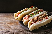 Assortment of homemade hot dogs with sausage, fried onion, tomatoes and cucumber, served on wood chopping board