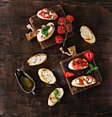 Assorted bruschetta with tomatoes, strawberries, feta cheese, chicken, mushrooms and basil on a wooden surface