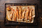 Grilled fried Tiger prawns shrimps on skewers and lemon on metal grid baking sheet background