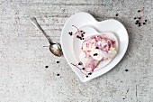 Vanilla ice cream with elderberry sauce on a heart-shaped plate (seen from above)