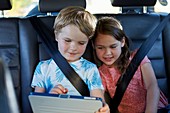 Brother and sister in car using tablet