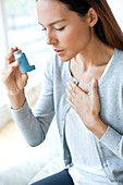 Young woman using inhaler touching chest