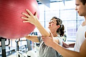 Trainer training woman with fitness ball