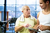 Gym trainer showing tablet to senior man