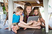 Three siblings under table with tablet