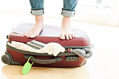 Woman packing,standing on full suitcase