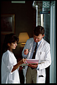 Doctor and nurse discuss records in hospital hall