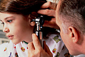 Doctor using otoscope to examine ear of young girl
