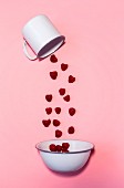Raspberries falling out of an enamel cup and into a bowl